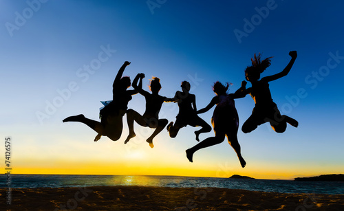 Teens jumping on the beach at sunset
