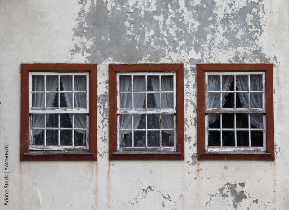 three windows on the shabby wall closed with curtains