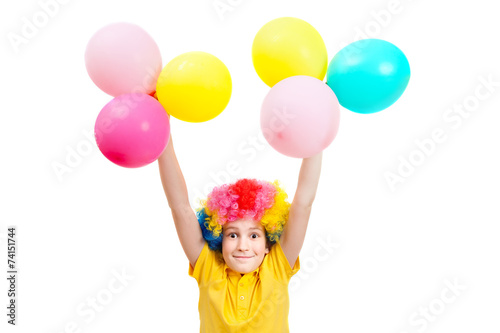 Smile boy in clown wig hands up with balloons