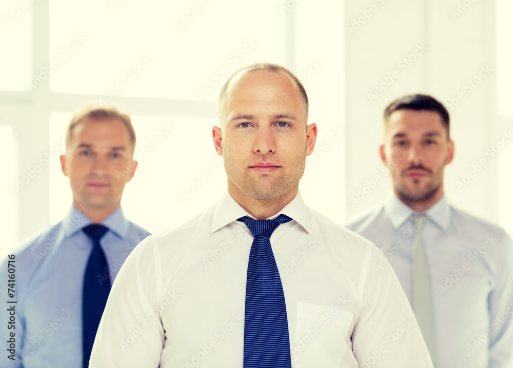 serious businessman in office with team on back serious businessman in office with team on back