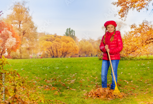Beautiful girl with rake cleans grass from leaves