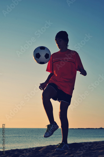 Boy playing football on beach