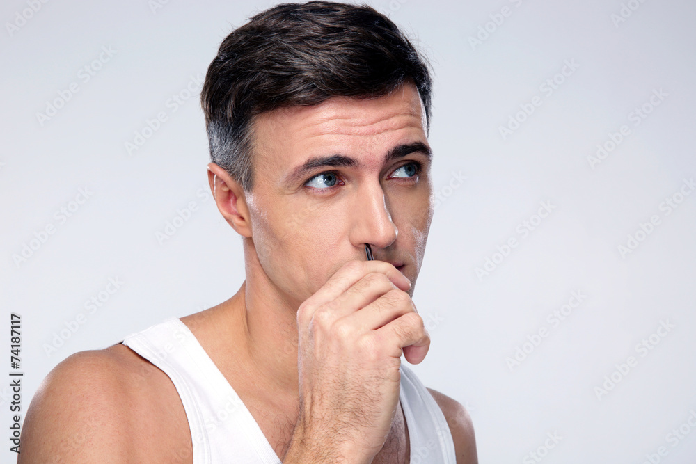 Man pucking nose hair with tweezers over gray background Man pucking nose hair with tweezers over gray background