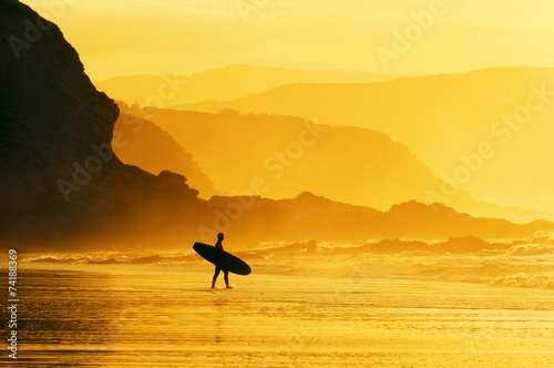surfer entering water at misty sunset photo