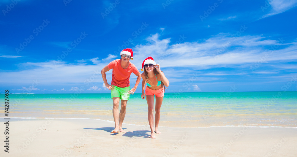 young couple in santa hats laughing on tropical beach. new year