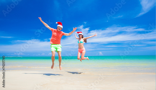 young couple in santa hats laughing on tropical beach. new year