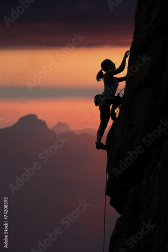 Elegant female climber ascents natural rock against sunset