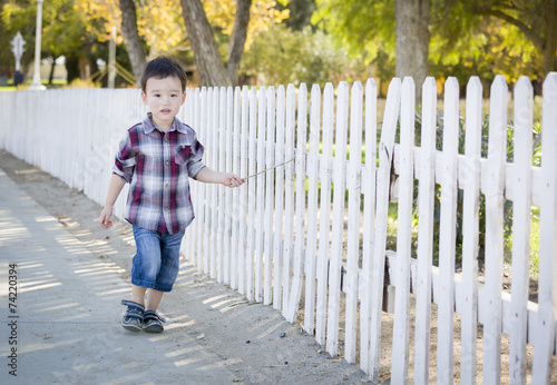 Young Mixed Race Boy Walking with Stick Along White Fence