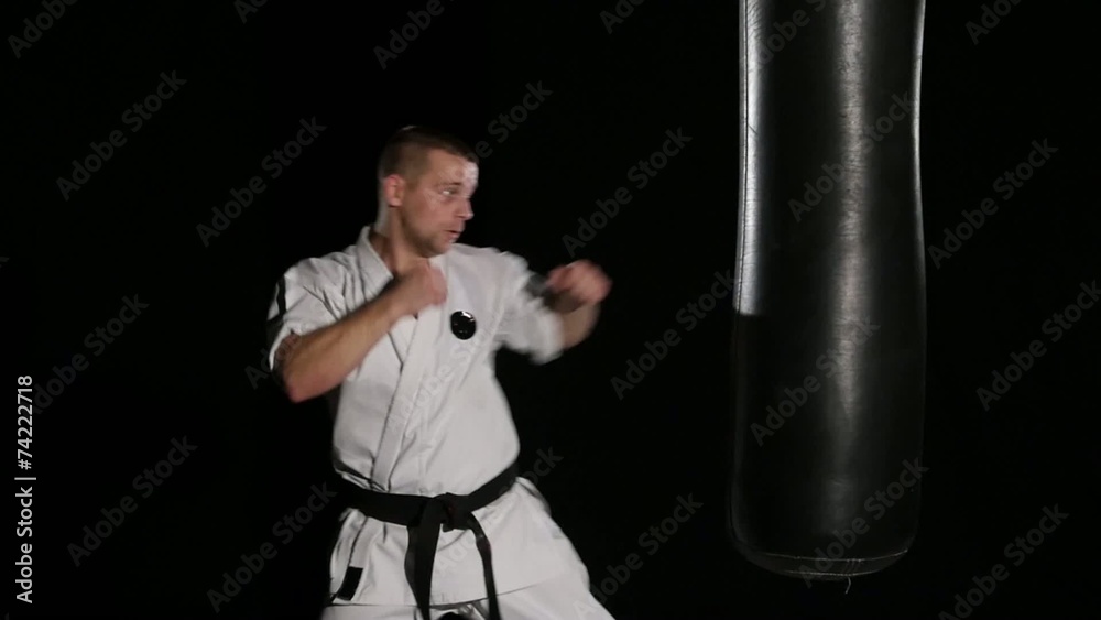 Black belt karate man practicing on the sandbag on black Black belt karate man practicing on the sandbag on black