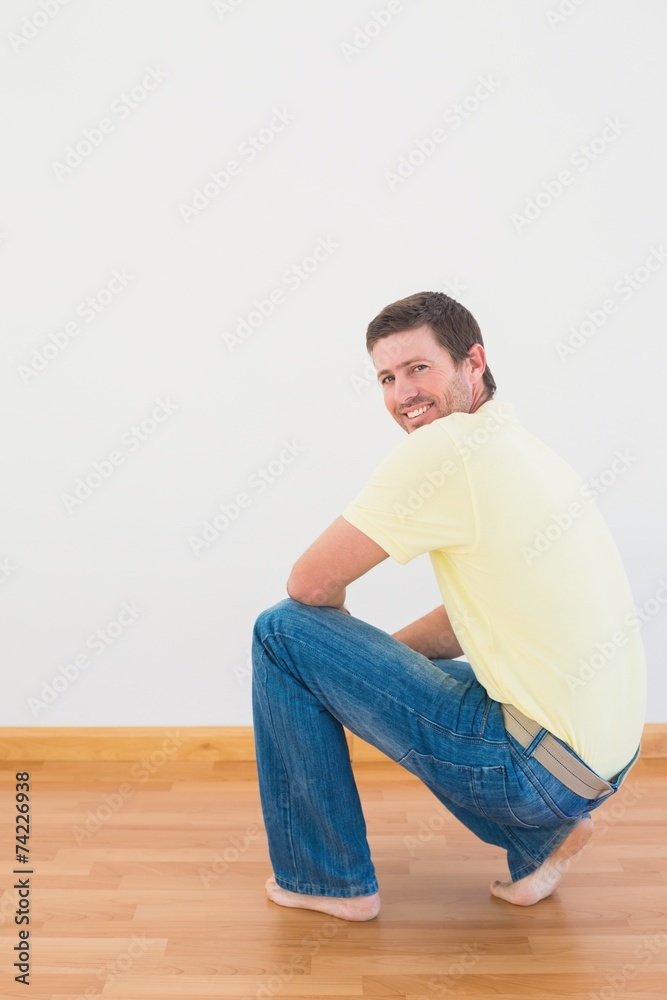 Casual man crouching on floor looking at wall at home Casual man crouching on floor looking at wall at home
