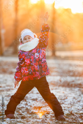Child standing in rays of setting sun with raised hand, winter
