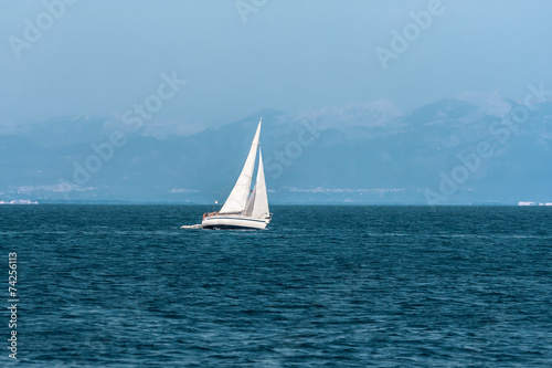 Sailboat floats quickly against the distant mountains
