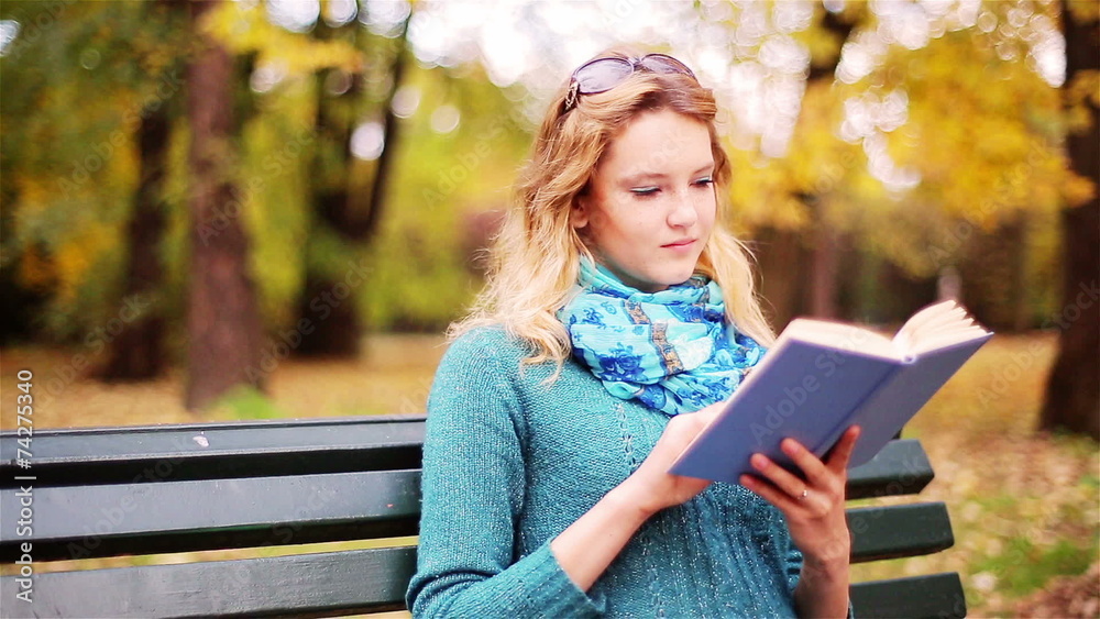 Girl reading book in the park and looking to the camera