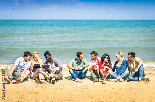 Group of multiracial best friends sitting and talking at beach