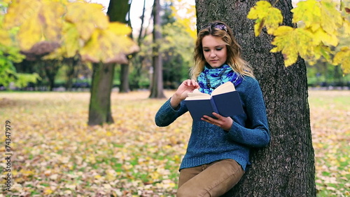 Pretty girl reading book and leaning on tree in the park photo