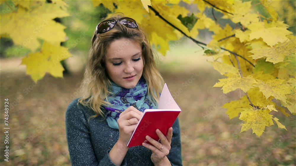 Happy girl doing notes in notebook in the park