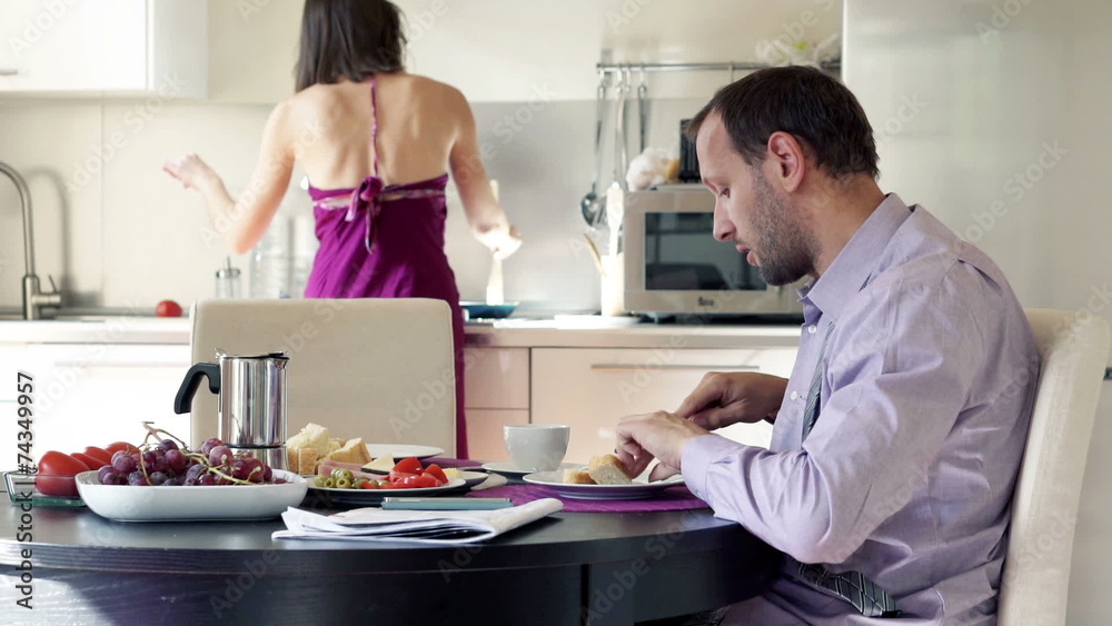 Man talking while his wife serving him breakfast in the kitchen Man talking while his wife serving him breakfast in the kitchen