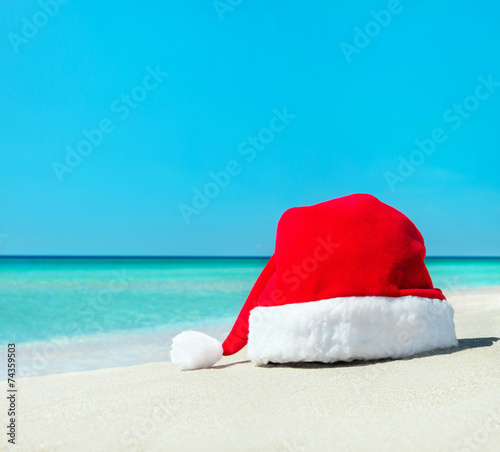 Santa christmas hat on white sand of tropical beach