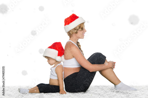 Mother and daughter sitting on snow in Santa hats