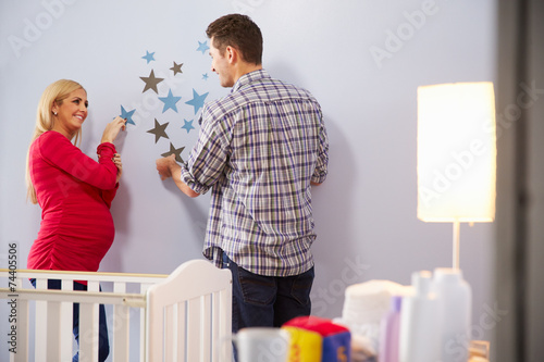 Couple With Pregnant Wife Adding Decorations To Nursery
