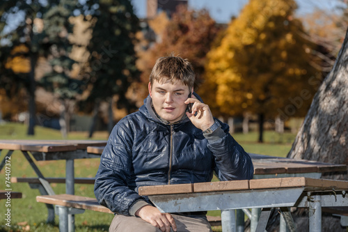 young adolescent sitting in park and communicating on cellphone