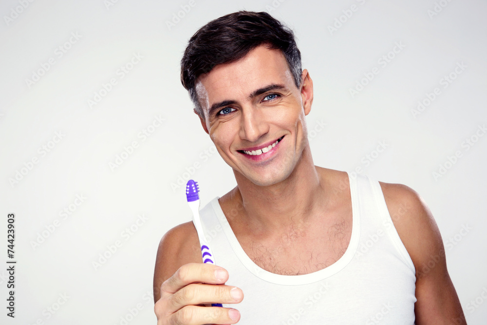 Happy man holding toothbrush on gray background Happy man holding toothbrush on gray background