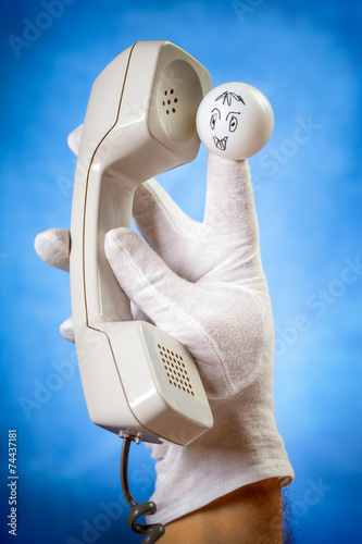 Finger puppet holding wired phone handset over blue background