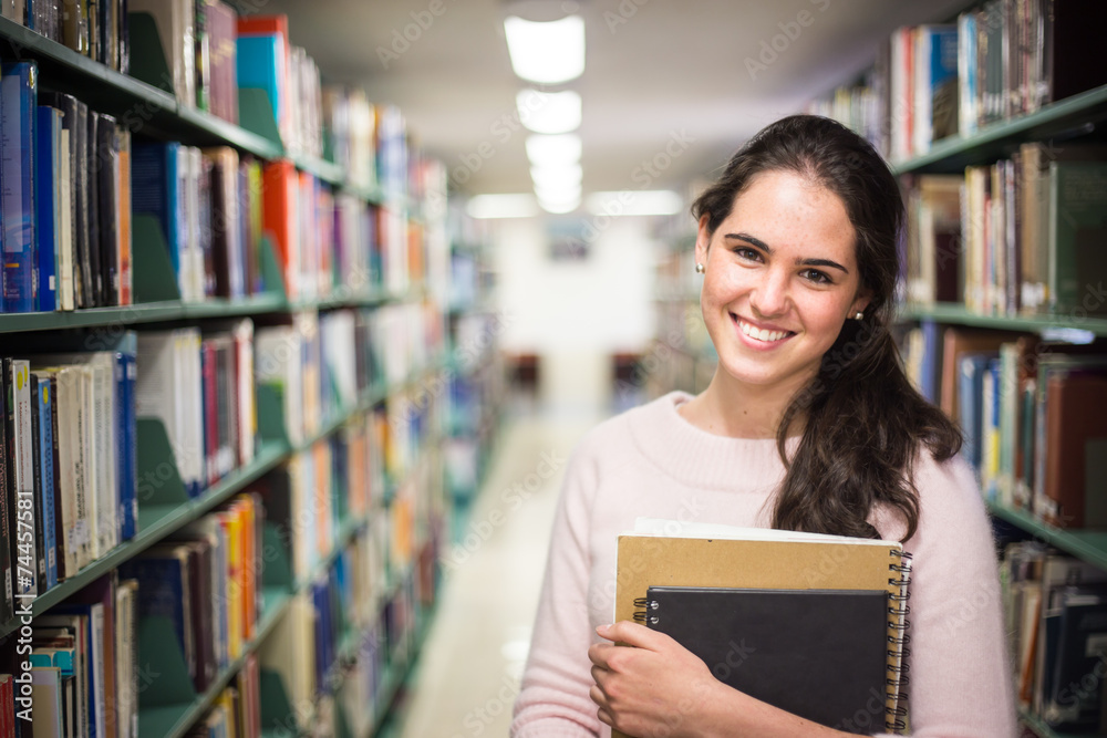 In the library - pretty female student with books working in a h In the library - pretty female student with books working in a h