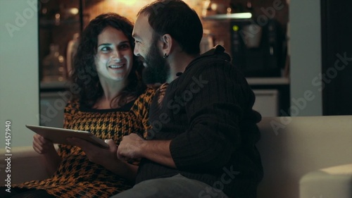 Couple using tablet on sofa at night in room