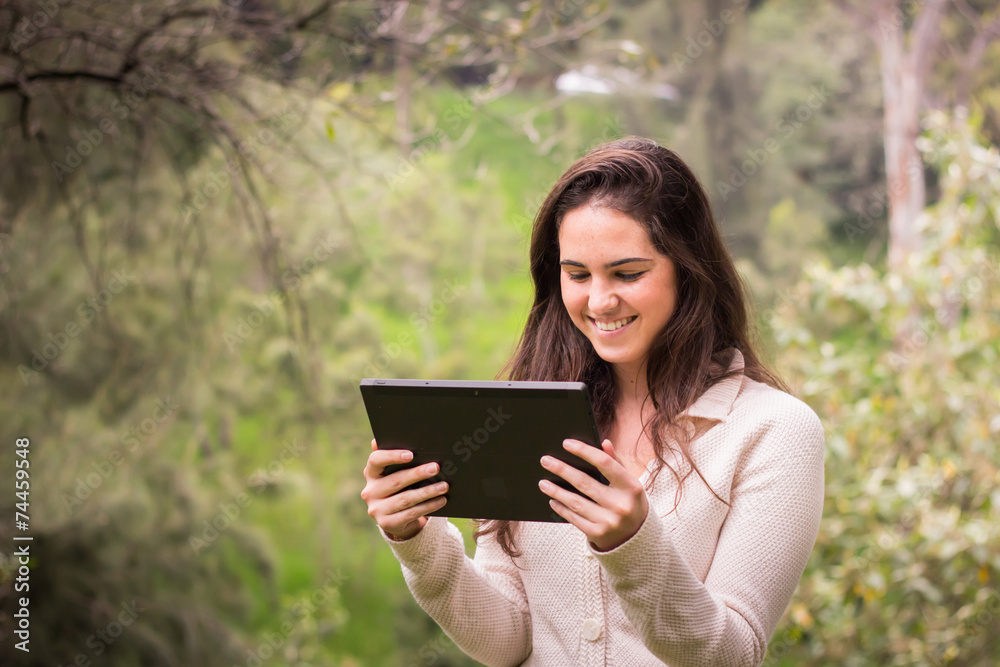 Young beautiful woman using a tablet computer at the park