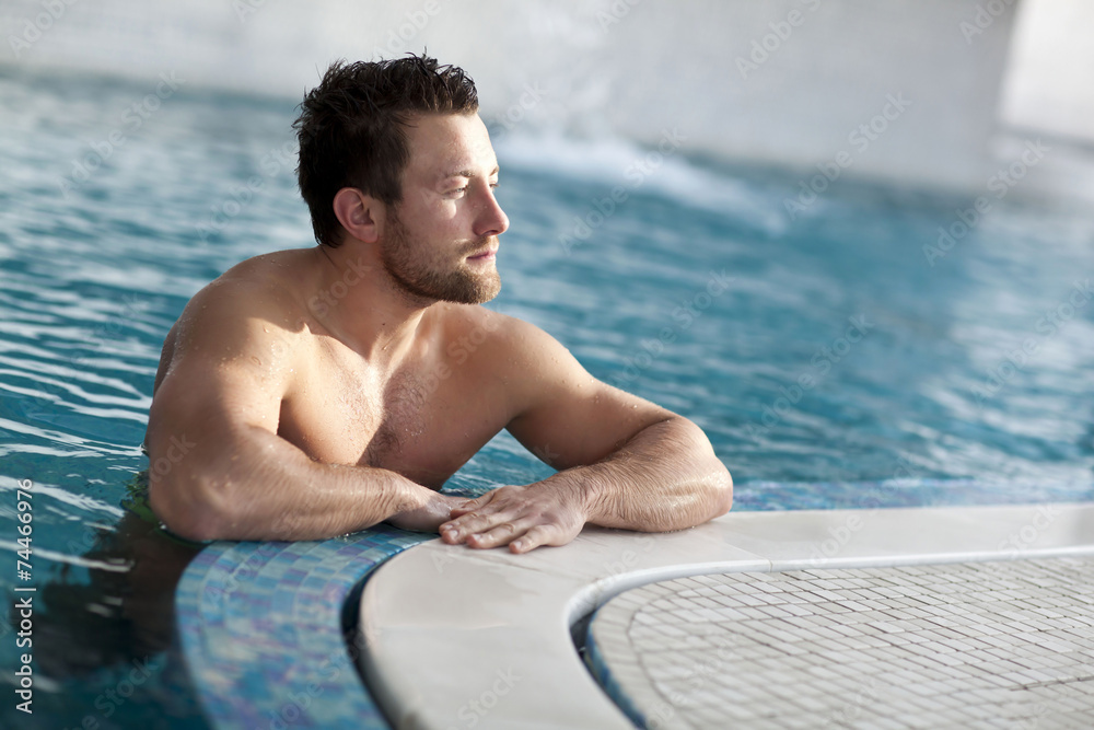 Young man leaning at edge of swimming pool 