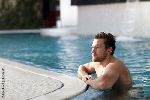 Young man leaning at edge of swimming pool 