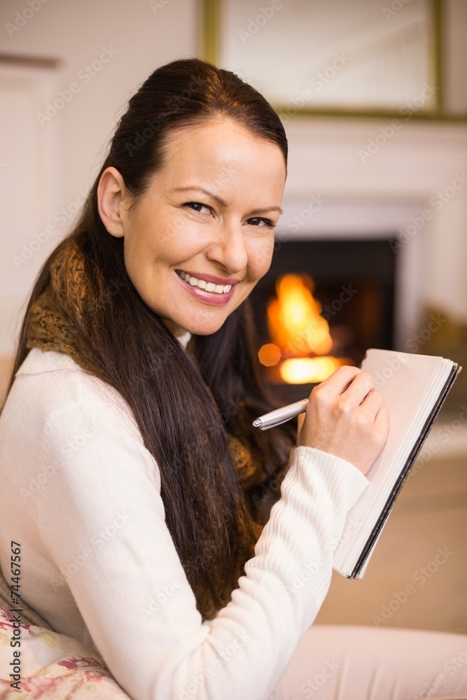 Smiling brunette sitting on the couch writing her christmas list Smiling brunette sitting on the couch writing her christmas list
