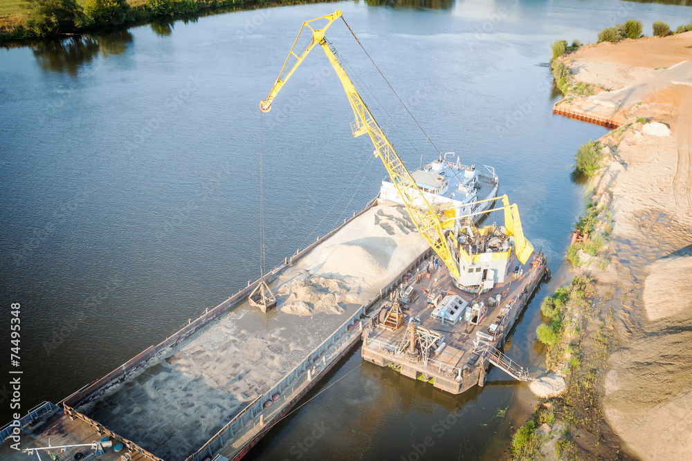 Floating jib crane during loading of sand on barge