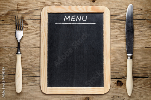 Blackboard menu, fork and knife on old wooden background