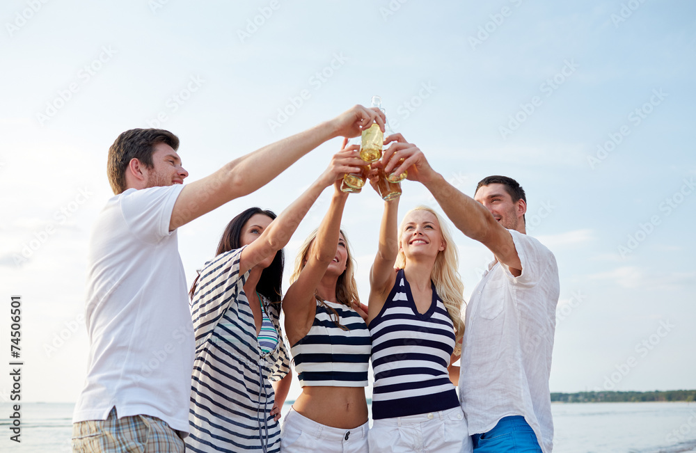 smiling friends clinking bottles on beach smiling friends clinking bottles on beach