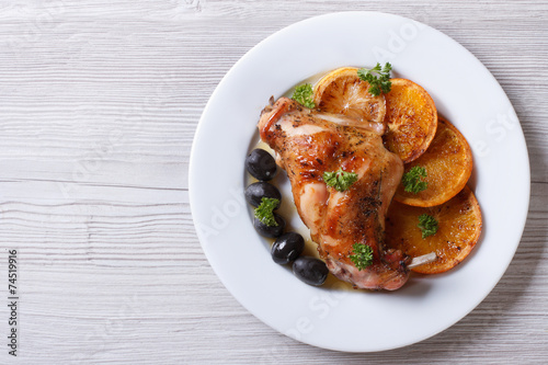 roasted rabbit leg with oranges on a white plate top view