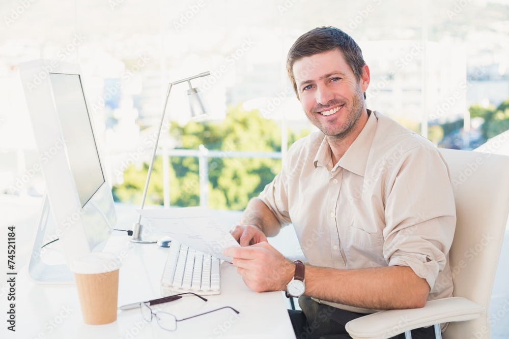 Smiling businessman looking at document at his desk