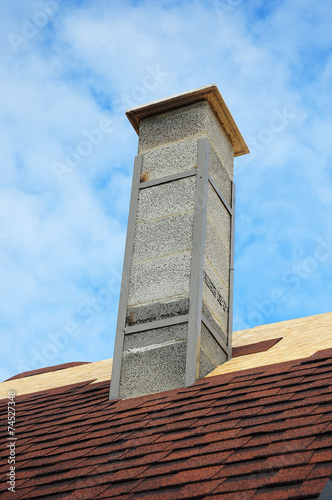 Roof under construction with new chimney against blue sky