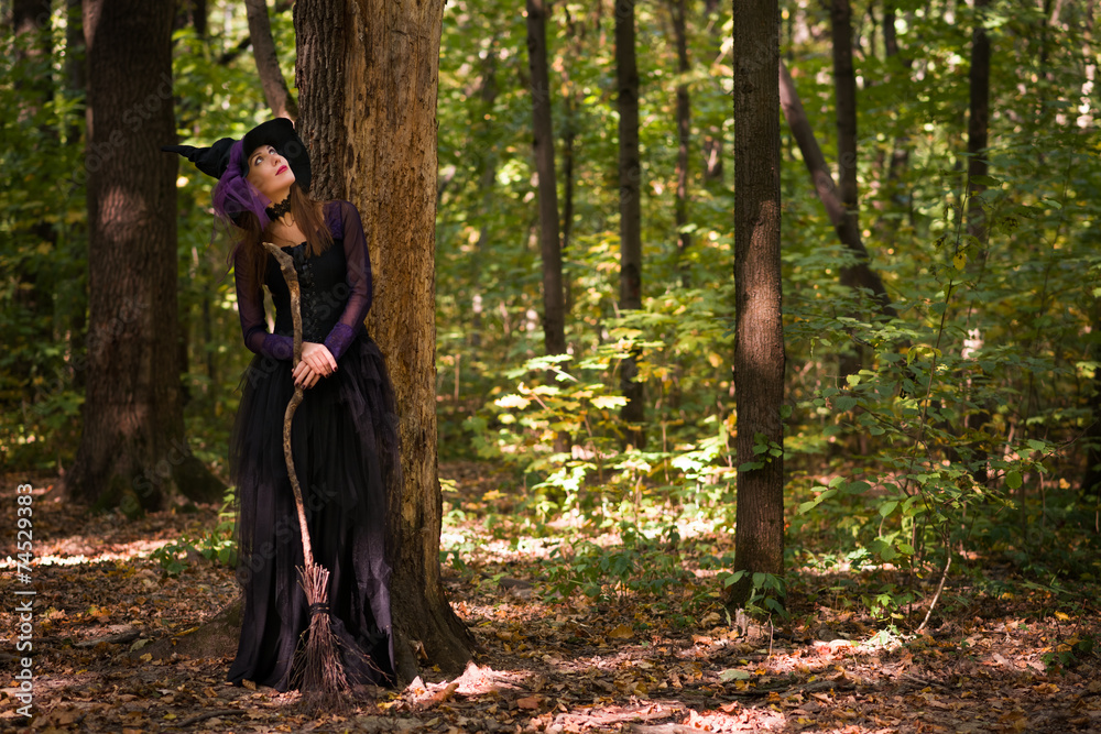 woman in witch's hat holding broom and looking upwards woman in witch's hat holding broom and looking upwards