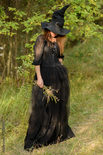 woman in black dress and witch's hat, weeds in hands