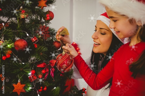 Mother and daughter hanging christmas decorations on tree
