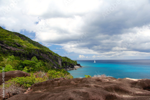 Rocky landscape in the Seychelles with sailboat in the distance