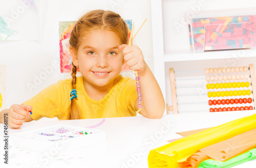 Little beautiful blond girl puts beads on string photo