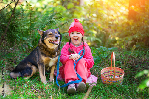 Happy little girl with dog relaxing in the forest