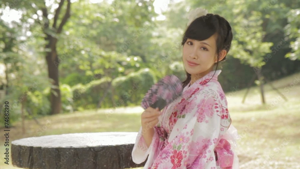 Asian woman in kimono fanning herself in Japanese garden Asian woman in kimono fanning herself in Japanese garden