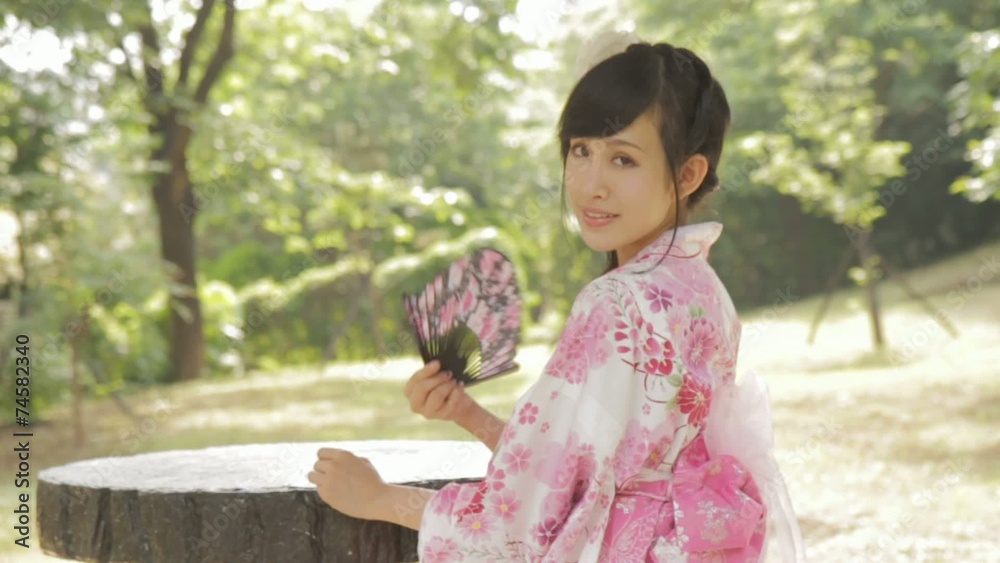 Asian woman in kimono fanning herself in Japanese garden Asian woman in kimono fanning herself in Japanese garden