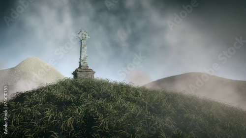 Grass hill with celtic cross from stone. Cloudy sky. photo