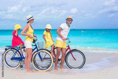 Young family of four with two kids riding bicycles on tropical