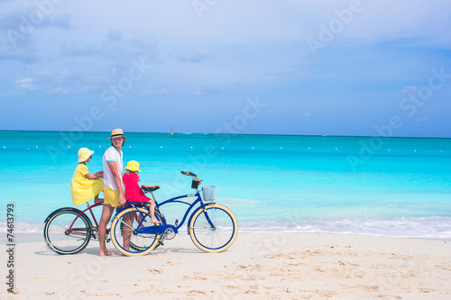 Happy dad and cute girls riding bicycles on tropical beach